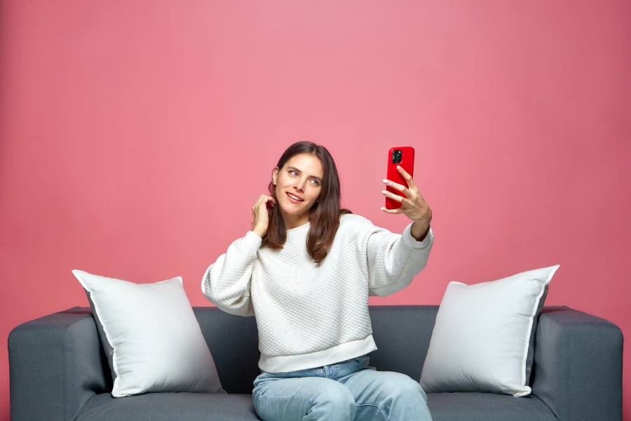Chica se hace un selfie en un sofá sobre fondo rosa